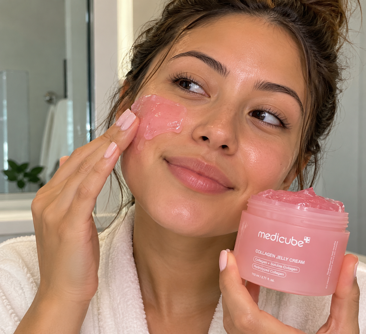 Person applying pink Medicube Collagen Jelly Cream to their cheek while holding the jar